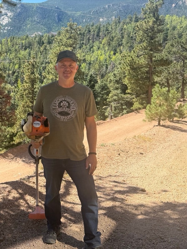 Jim outside holding a Stihl string trimmer, mountains behind him