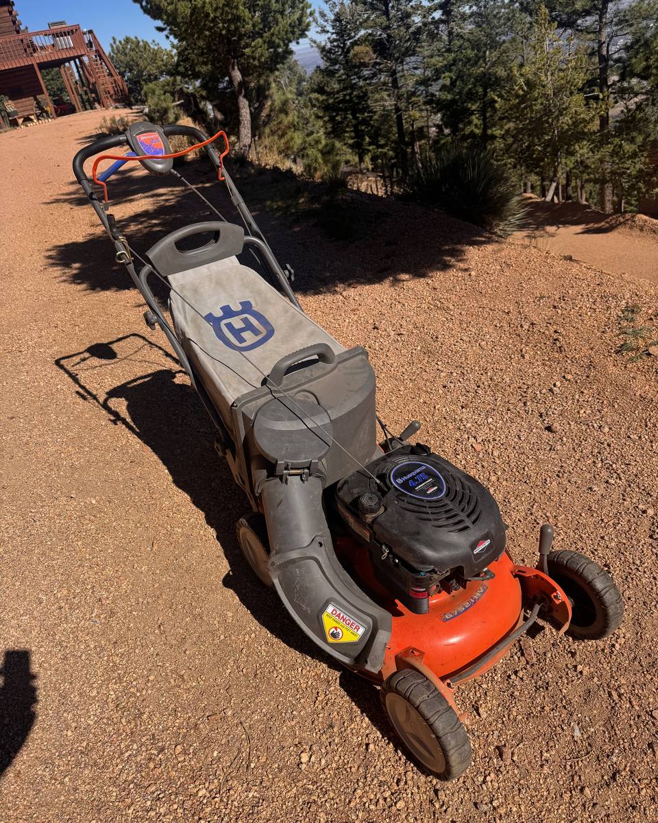 Orange Husqvarna self-propelled mower with its bagger on a gravel drive